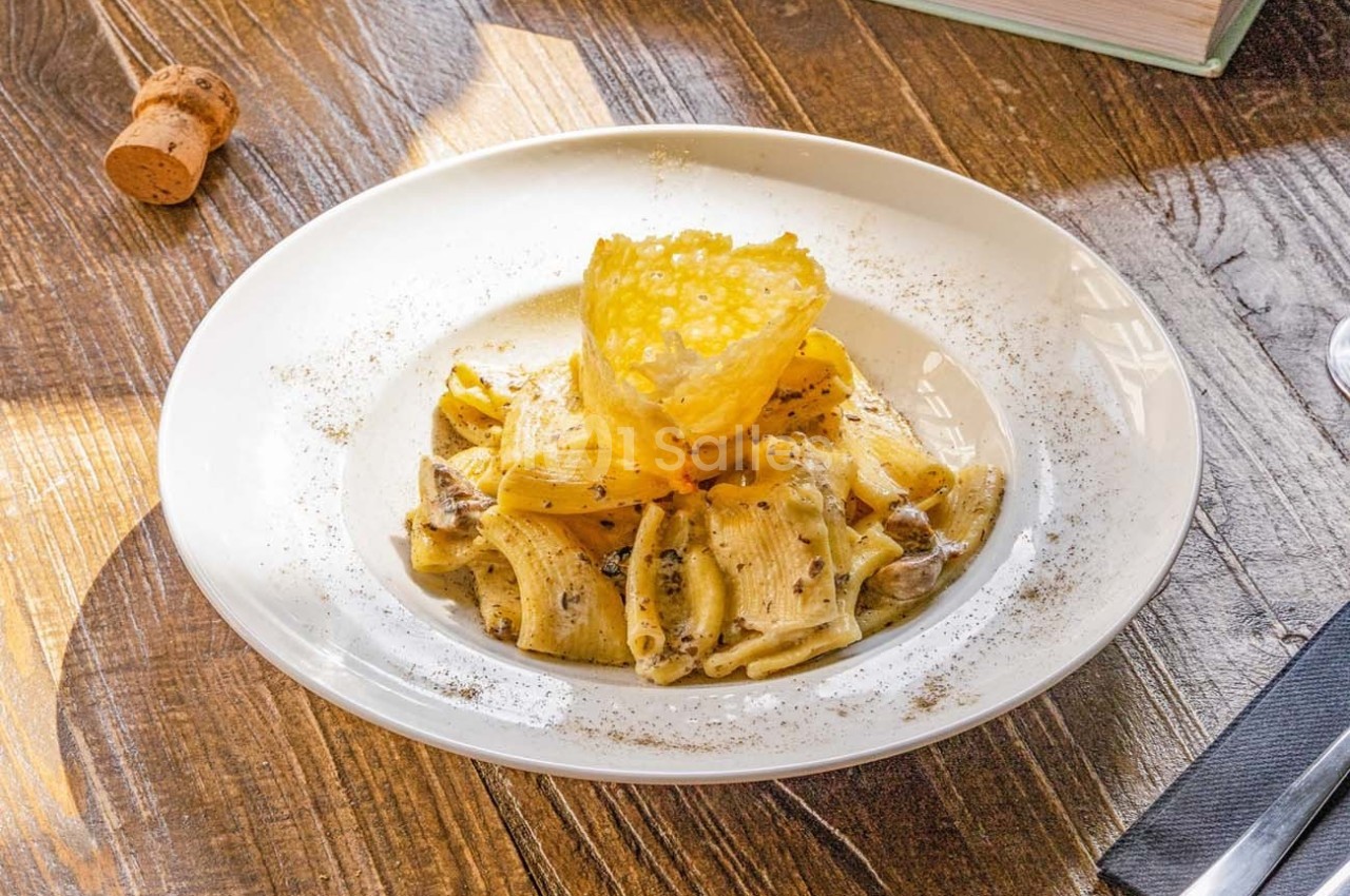 Assiette de pâtes rigatoni à la truffe avec une tuile de parmesan, servie sur une table en bois.
