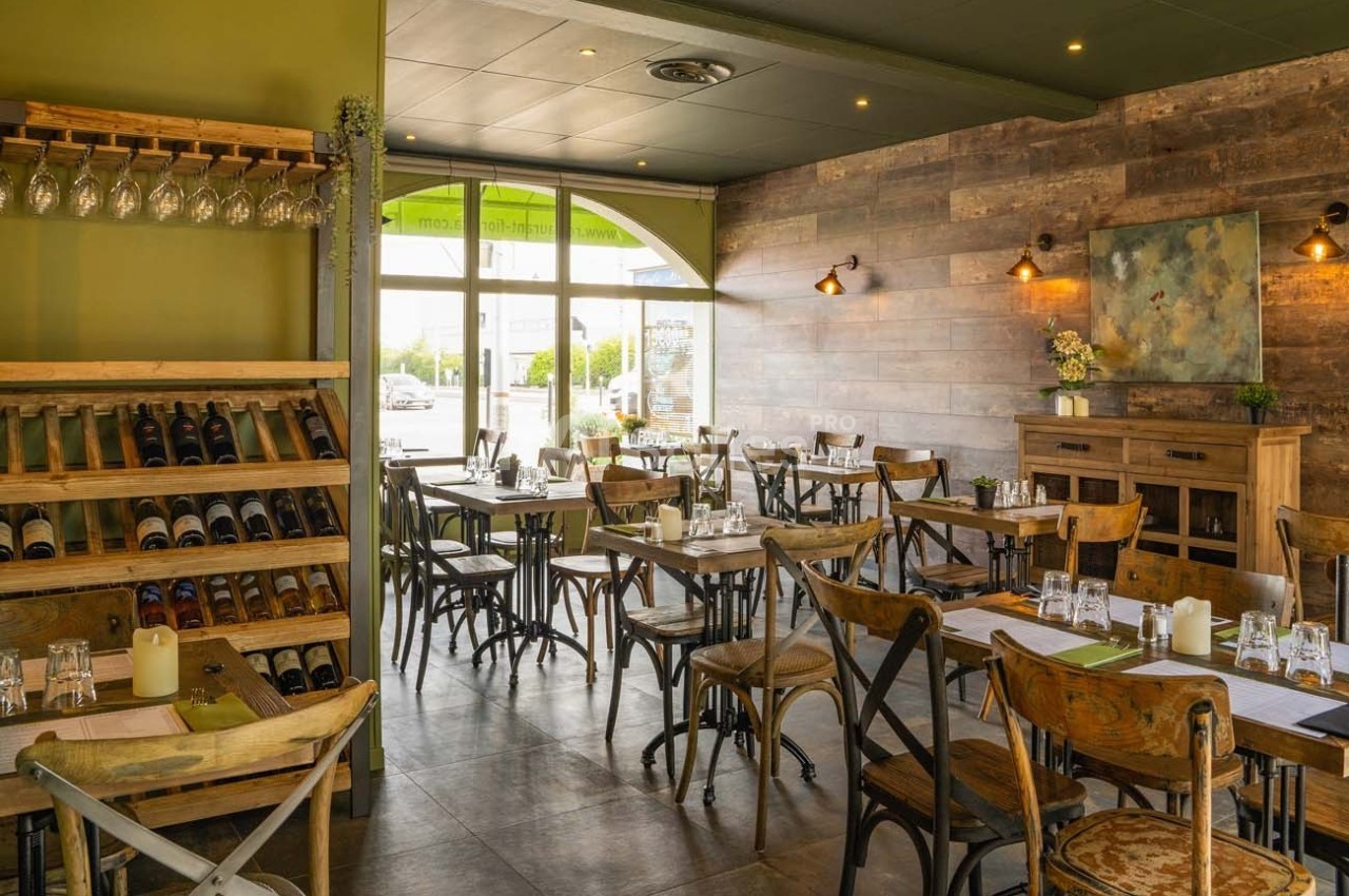 Salle de restaurant lumineuse avec tables en bois, chaises assorties, étagères à vin et décoration murale chaleureuse.