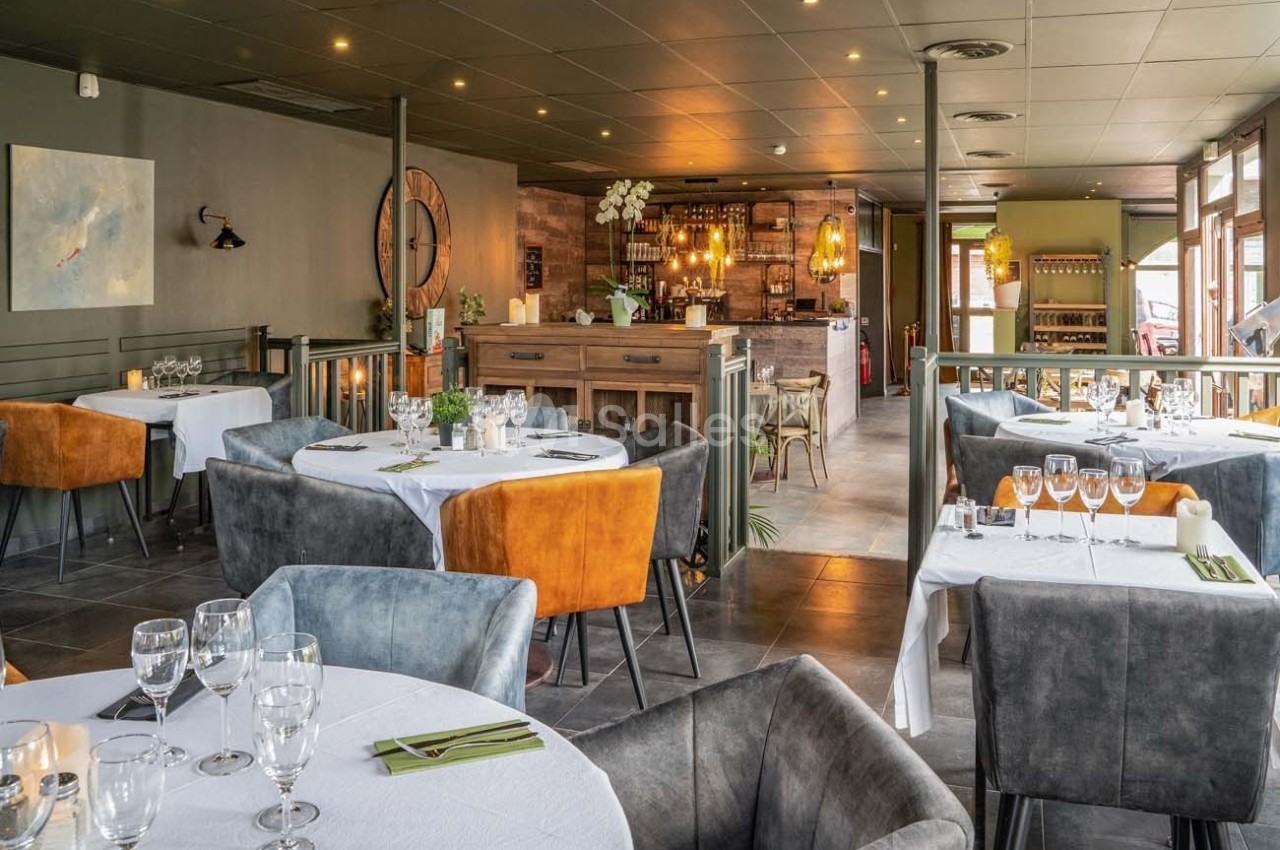 Salle de restaurant élégante avec tables dressées, chaises colorées et un bar en bois au fond.