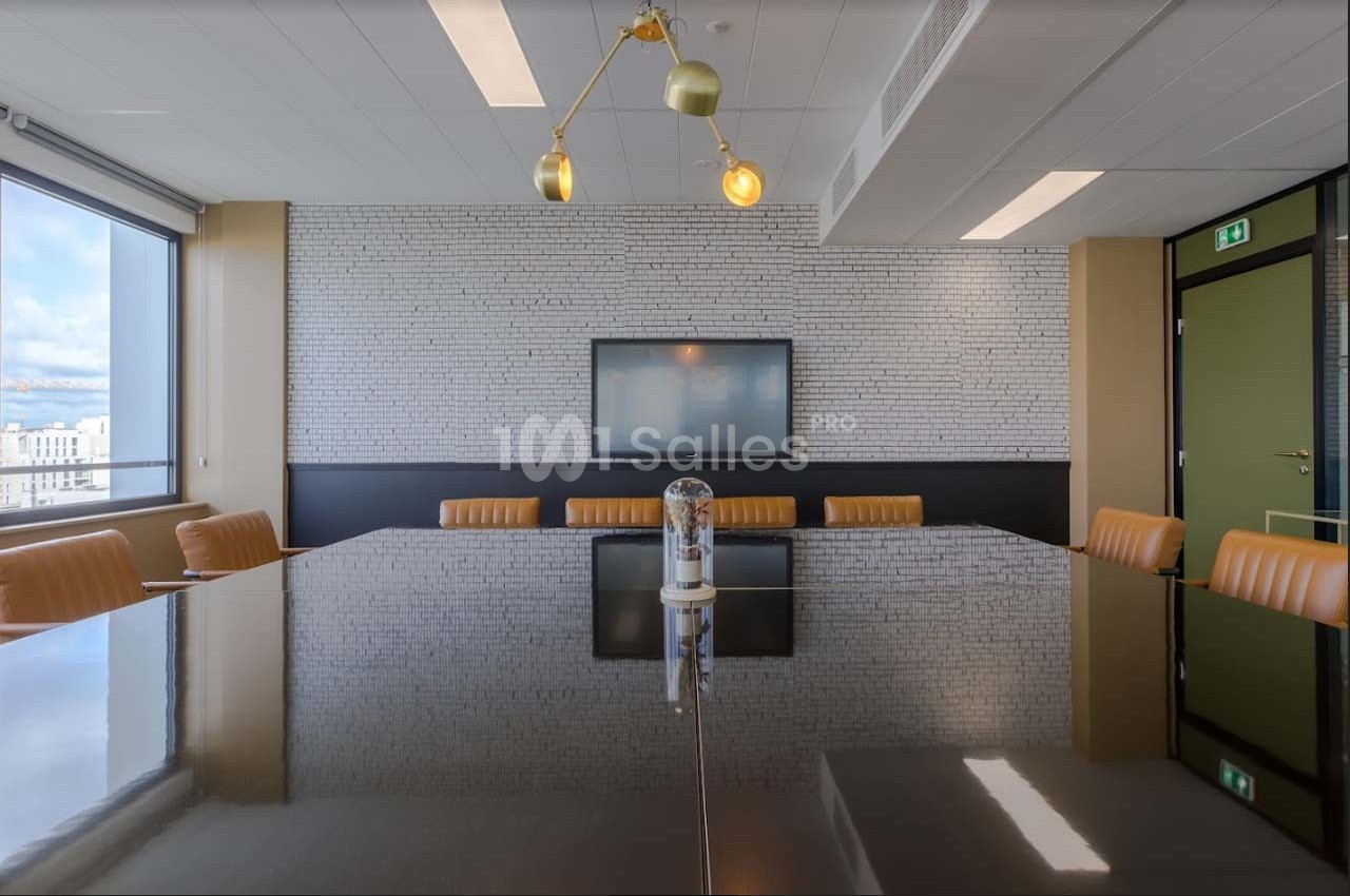Salle de réunion moderne avec table en bois sombre, chaises en cuir orange, écran mural et éclairage suspendu.