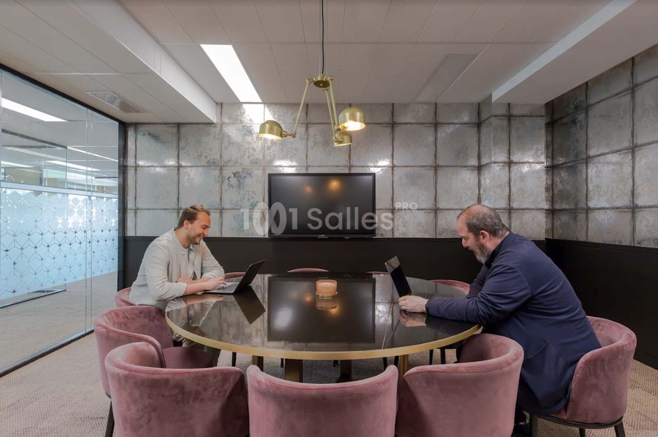 Deux hommes travaillent sur des ordinateurs portables autour d'une table ronde dans une salle de réunion moderne.