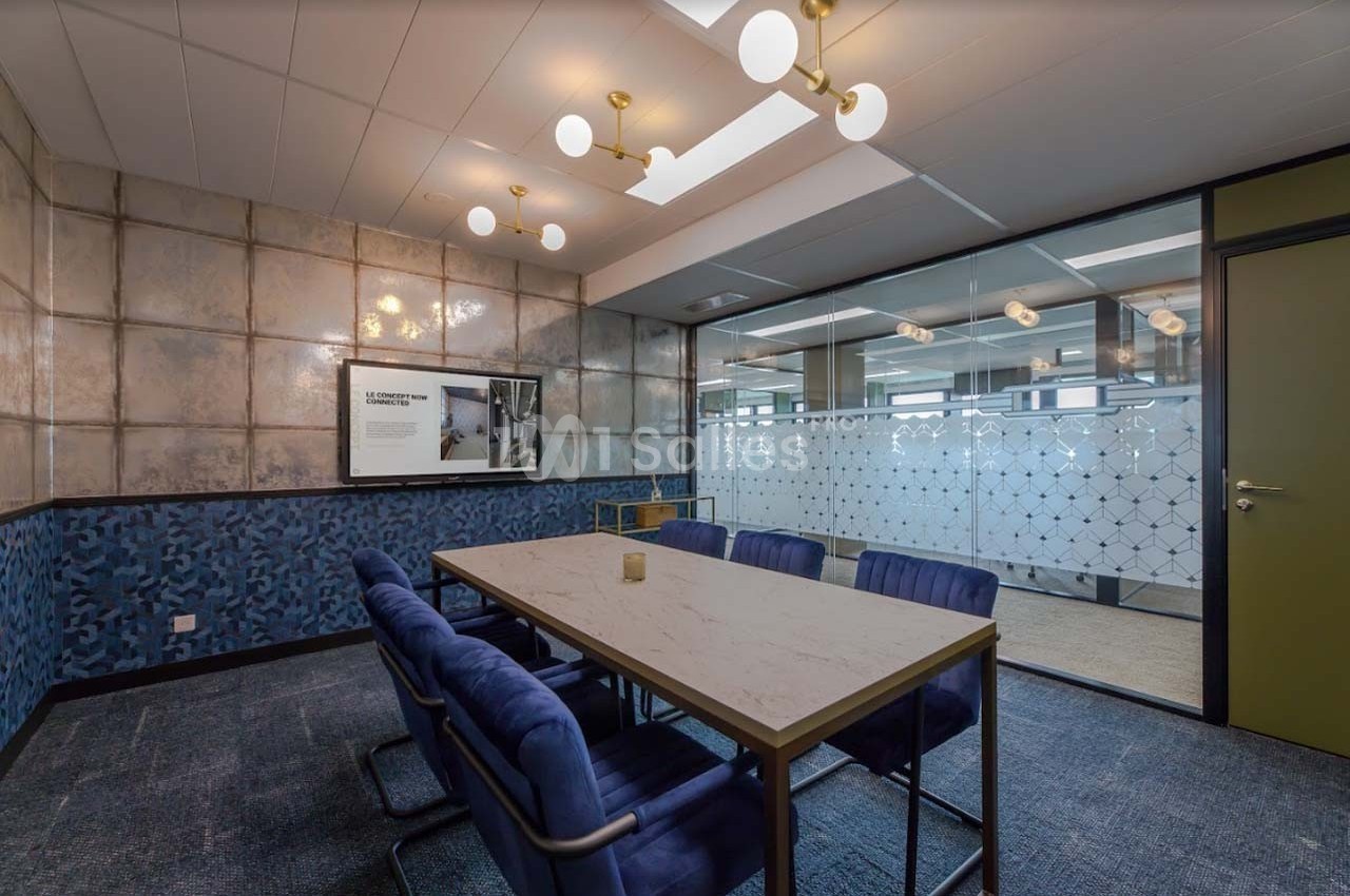 Salle de réunion moderne avec table en marbre, chaises bleues, écran mural et cloison vitrée décorative.