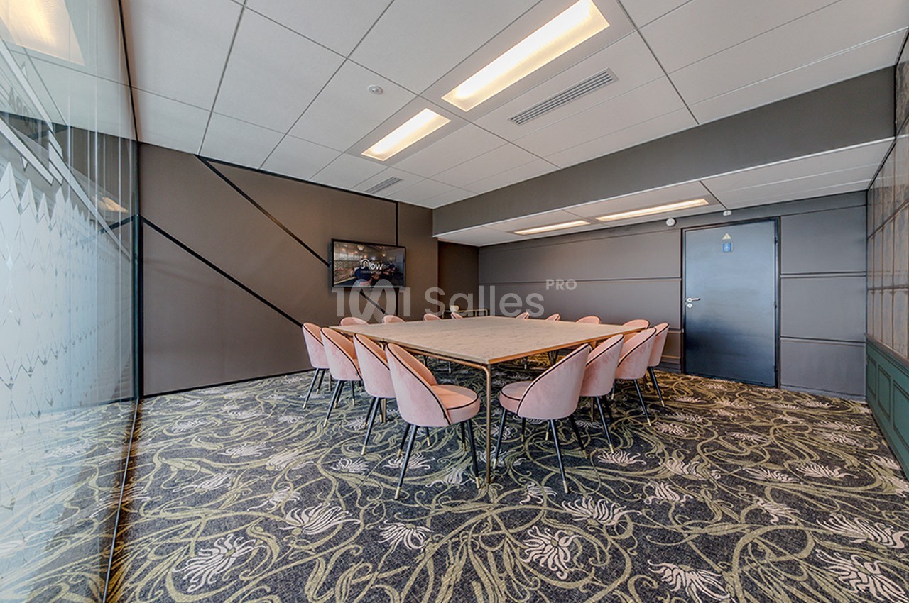 Salle de réunion moderne avec une grande table rectangulaire entourée de chaises roses, éclairée par des plafonniers.