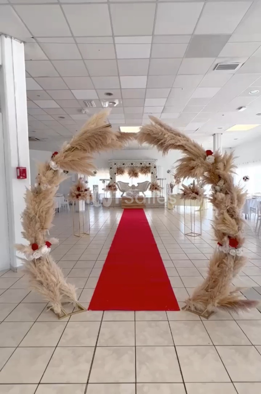 Arche décorative en pampas avec tapis rouge menant à une salle de réception lumineuse et aménagée.