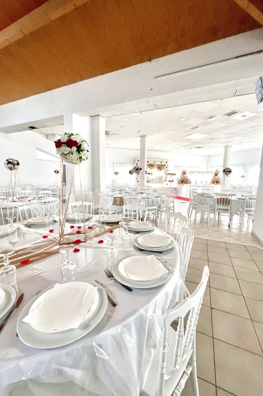 Salle de réception décorée avec des tables rondes dressées, nappes blanches et centres de table fleuris.