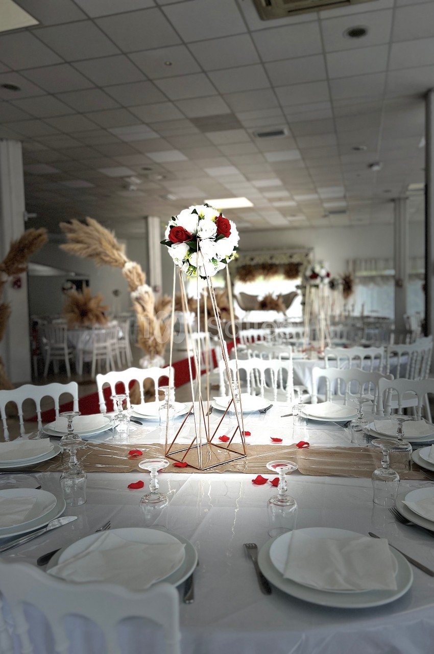 Salle de réception décorée avec des tables dressées, un centre de table floral et des éléments en pampas en arrière-plan.