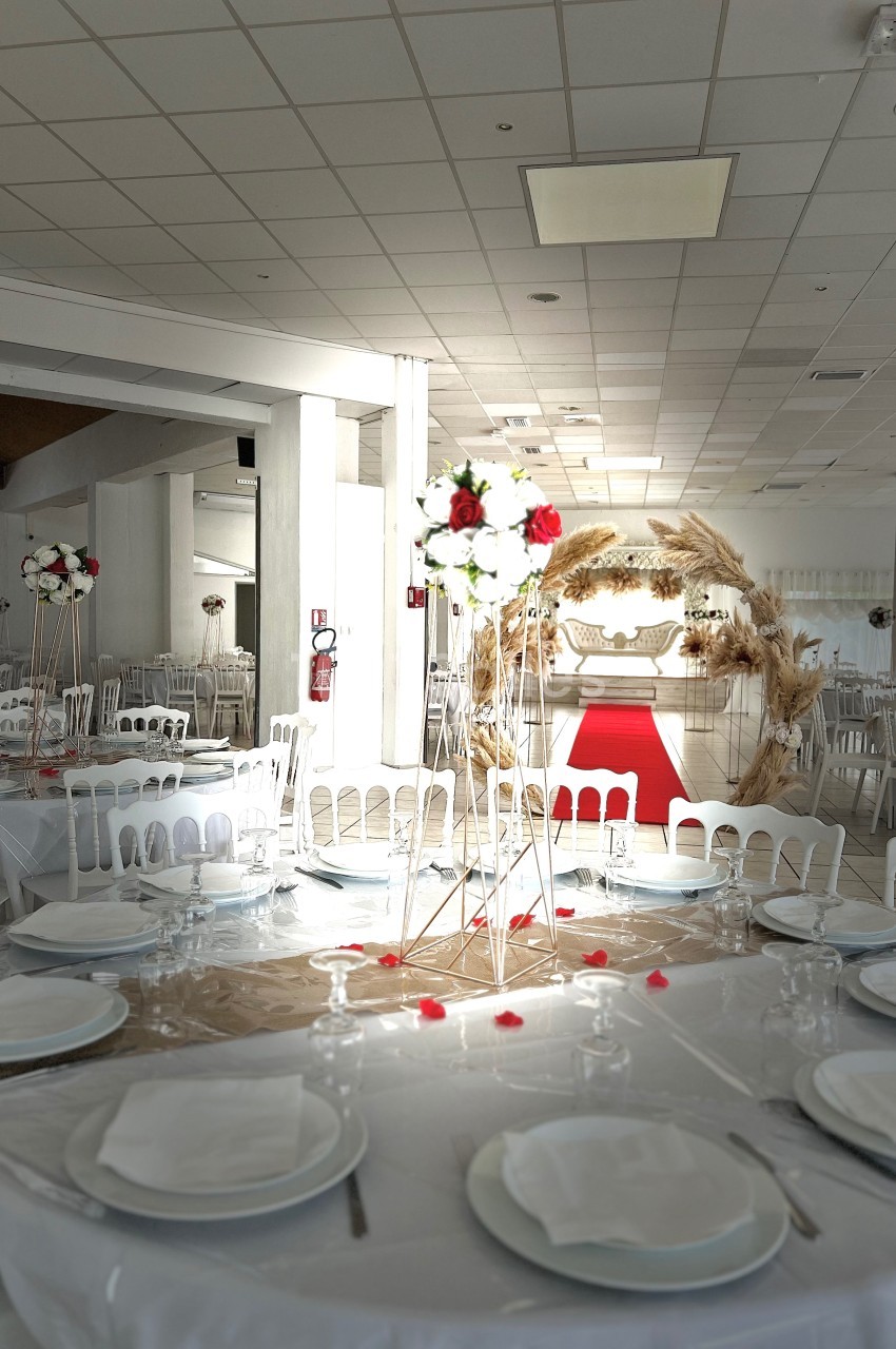 Salle de réception décorée avec des tables dressées, des chaises blanches et une arche florale près d'un tapis rouge.