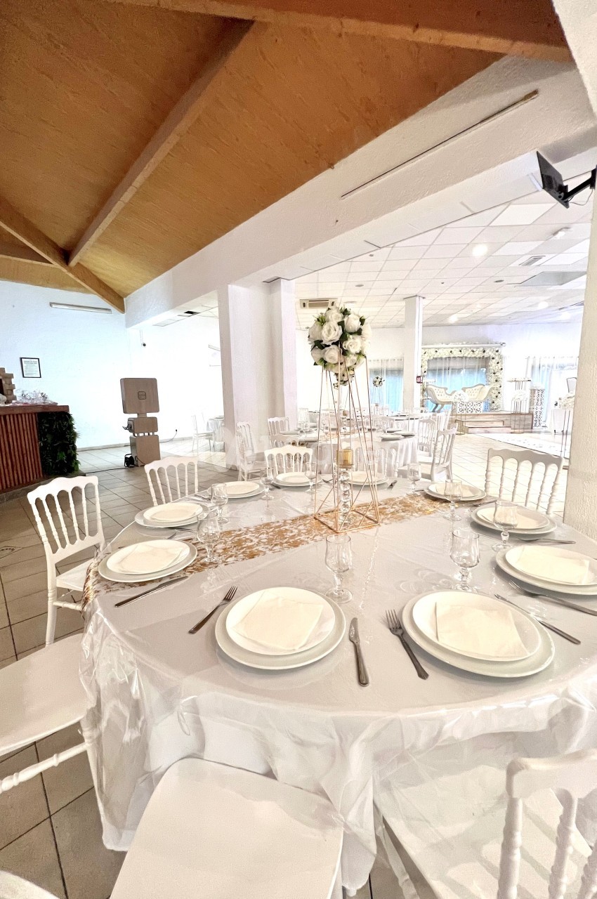 Salle de réception décorée avec une table ronde dressée, nappes blanches, chaises assorties et un centre de table floral.