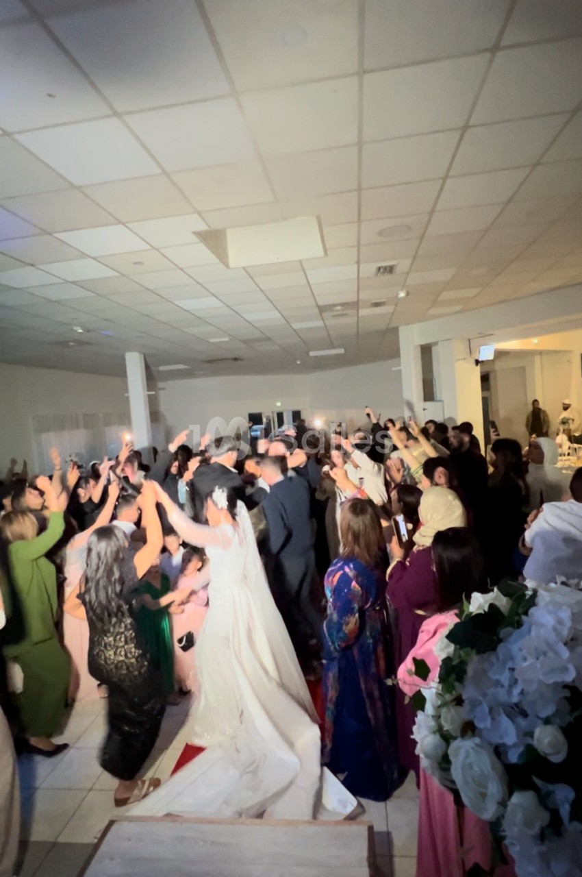 Des invités dansent et célèbrent dans une salle de réception éclairée, avec une mariée en robe blanche au premier plan.