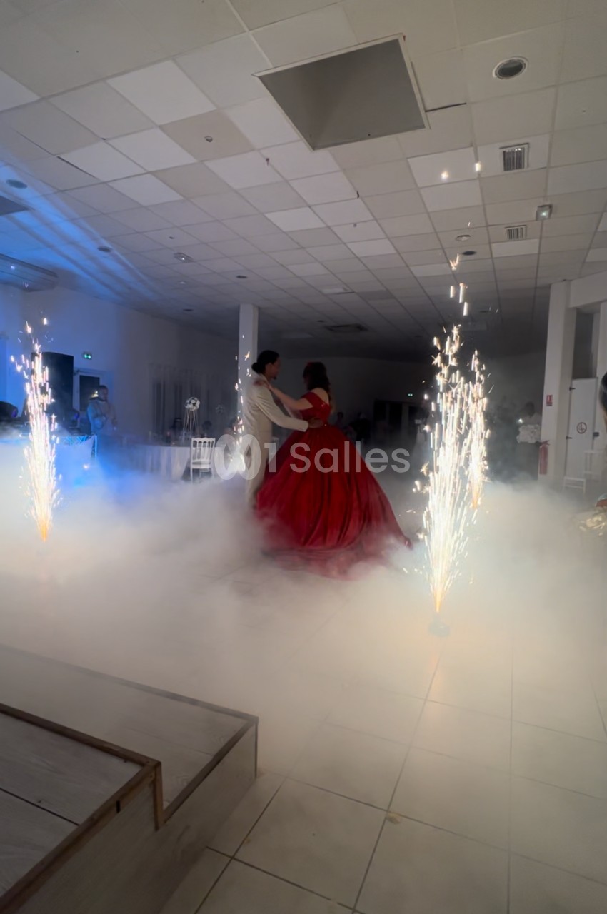 Un couple danse au centre d'une salle illuminée, entouré de fumée et de fontaines d'étincelles.