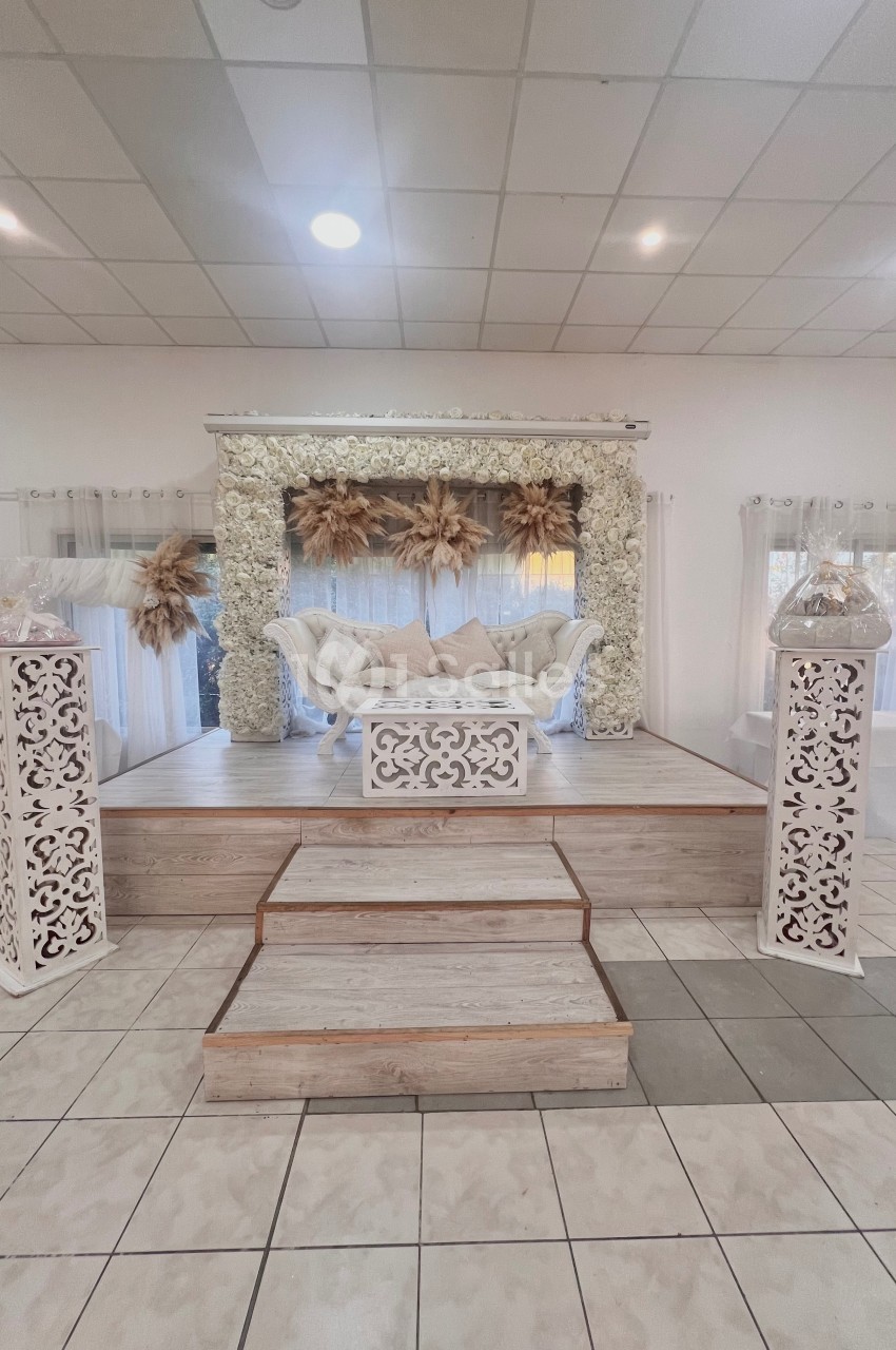 Estrade décorée avec un canapé blanc, des fleurs séchées et des éléments floraux sous un dais lumineux.
