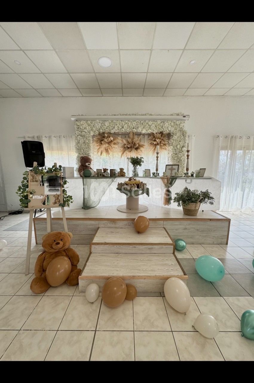 Décoration de salle avec ballons, ours en peluche et fleurs séchées sur une estrade, ambiance douce et lumineuse.