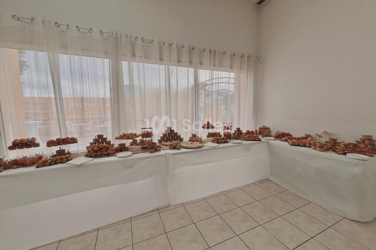 Table garnie de pâtisseries variées disposées sur des présentoirs dans une salle lumineuse avec de grandes fenêtres.