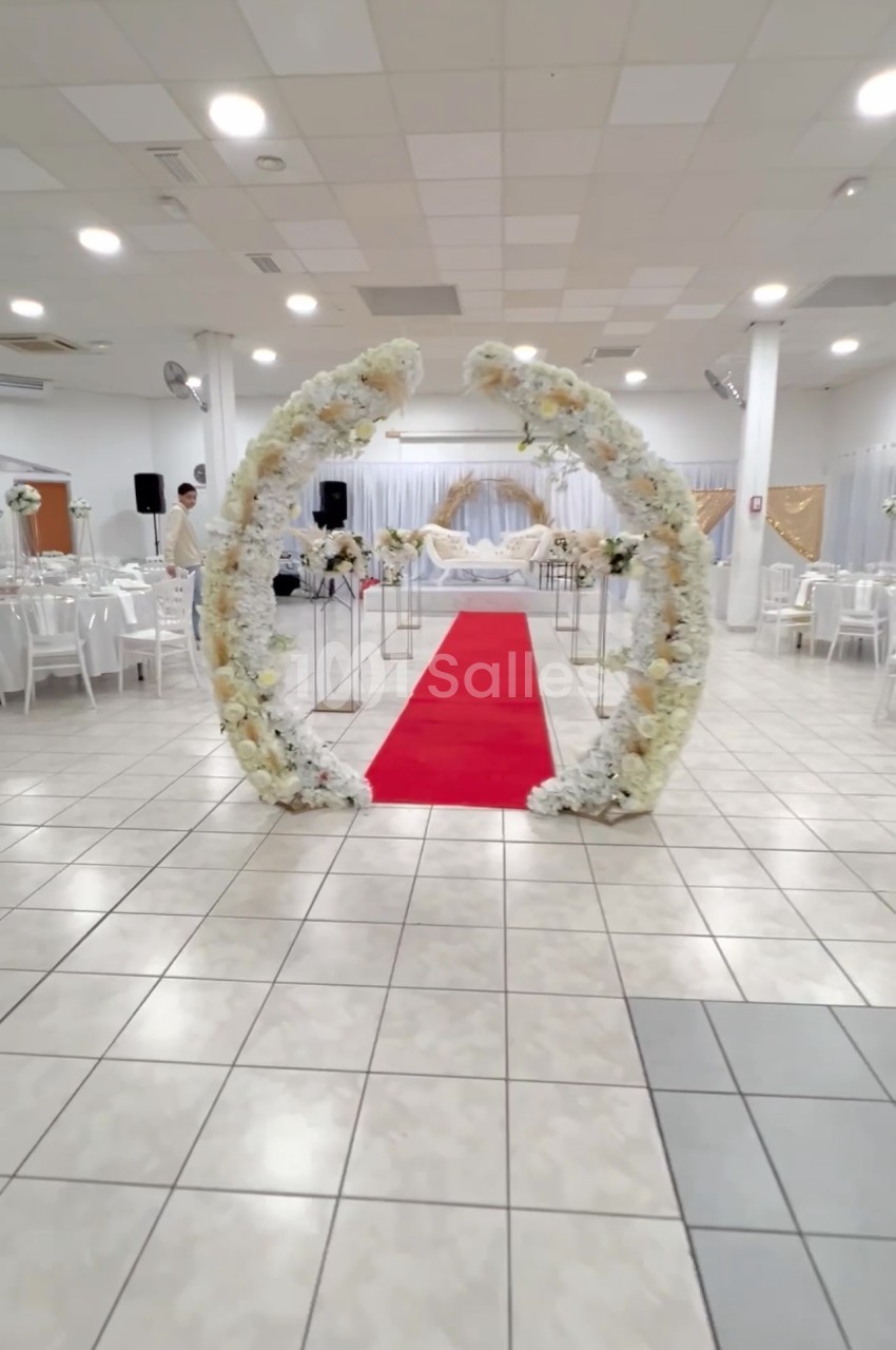 Arche florale blanche entourant un tapis rouge dans une salle de réception décorée pour un événement.