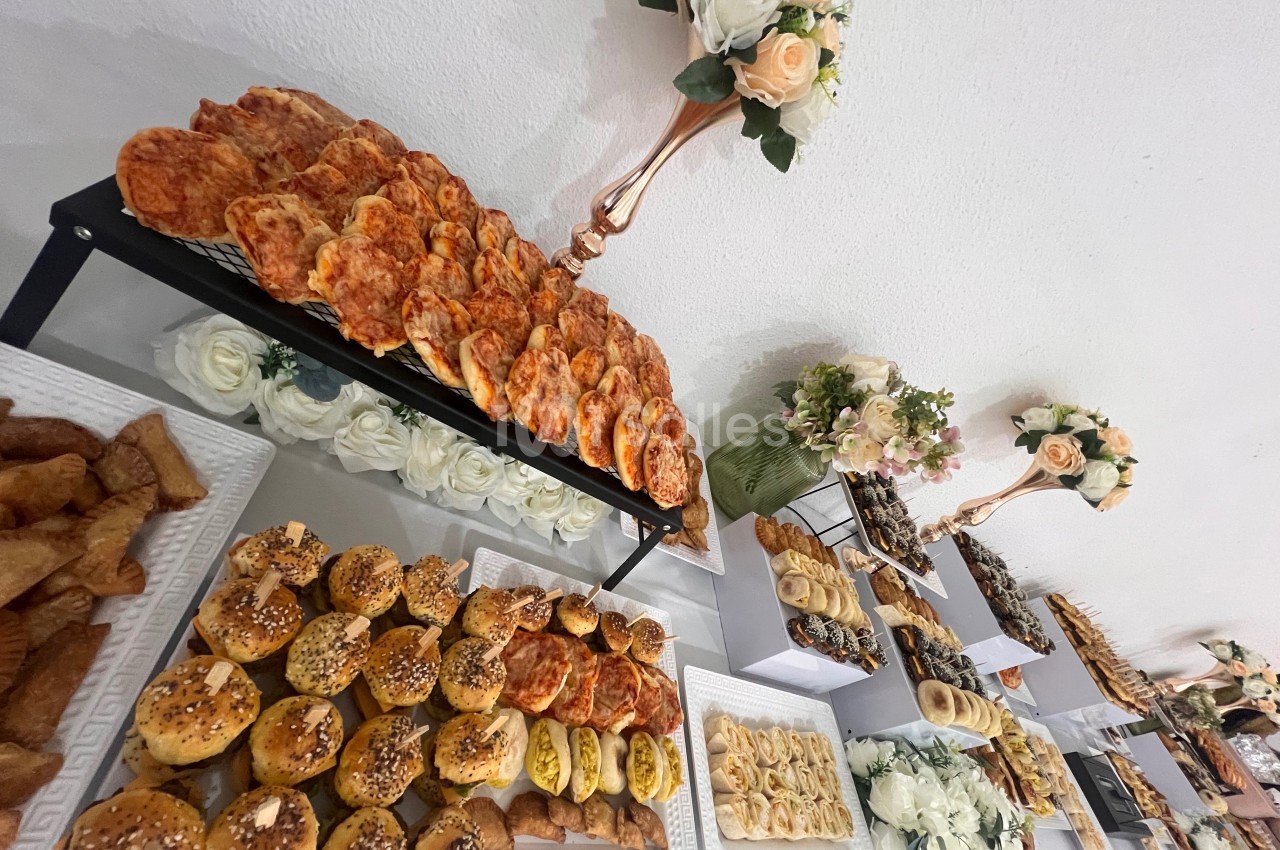 Buffet composé de viennoiseries salées, pains garnis et décorations florales sur une table blanche.