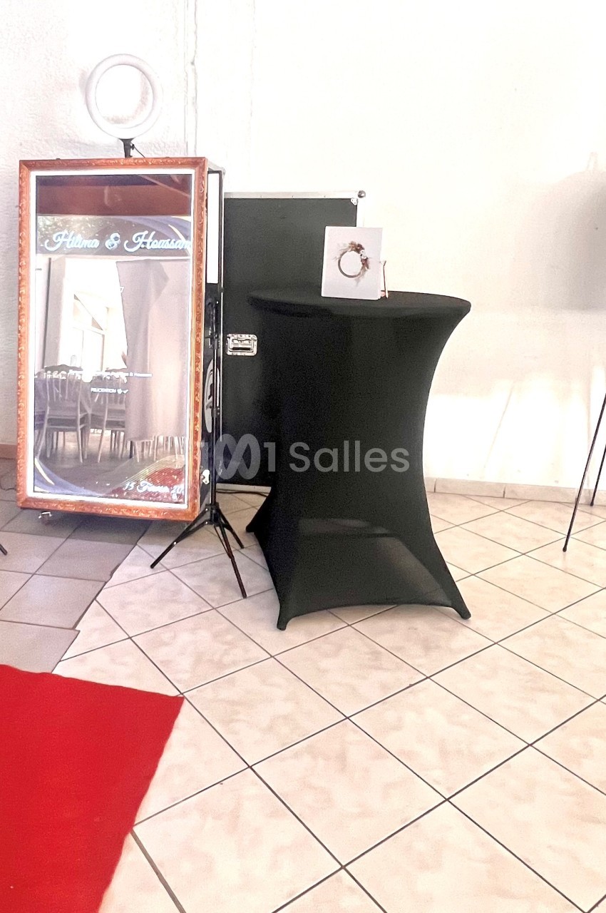 Miroir photobooth entouré d'équipements sur trépieds, avec une table noire et un chevalet dans une pièce carrelée.