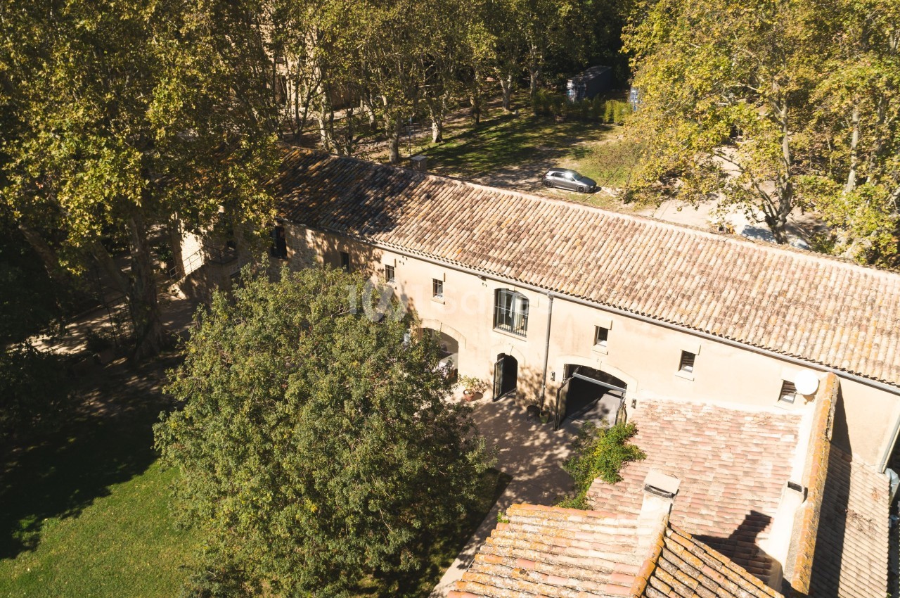 Vue aérienne d'un bâtiment ancien en pierre entouré d'arbres et d'une pelouse, avec une route à proximité.
