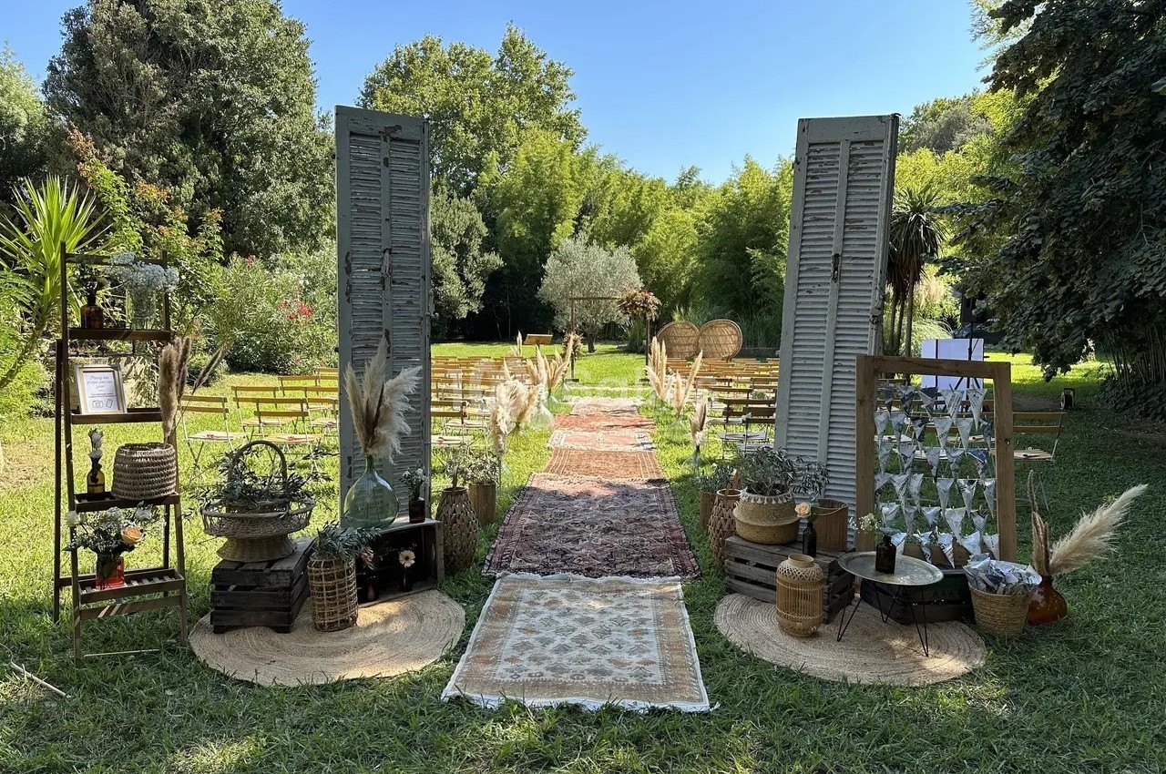 Allée centrale décorée de tapis et d'objets rustiques menant à des chaises disposées pour une cérémonie en plein air.