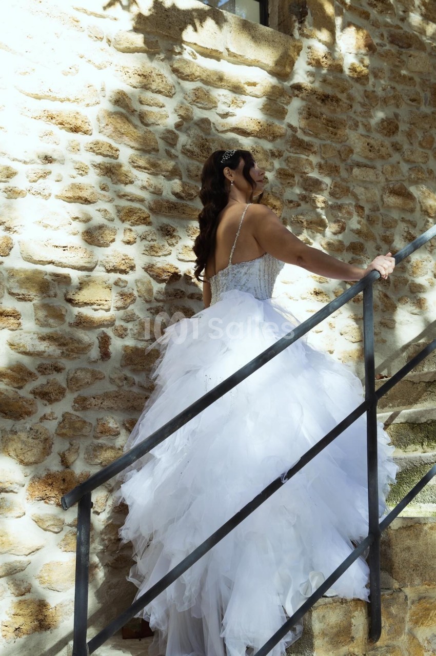 Femme en robe de mariée blanche montant un escalier en pierre, éclairée par une lumière naturelle.