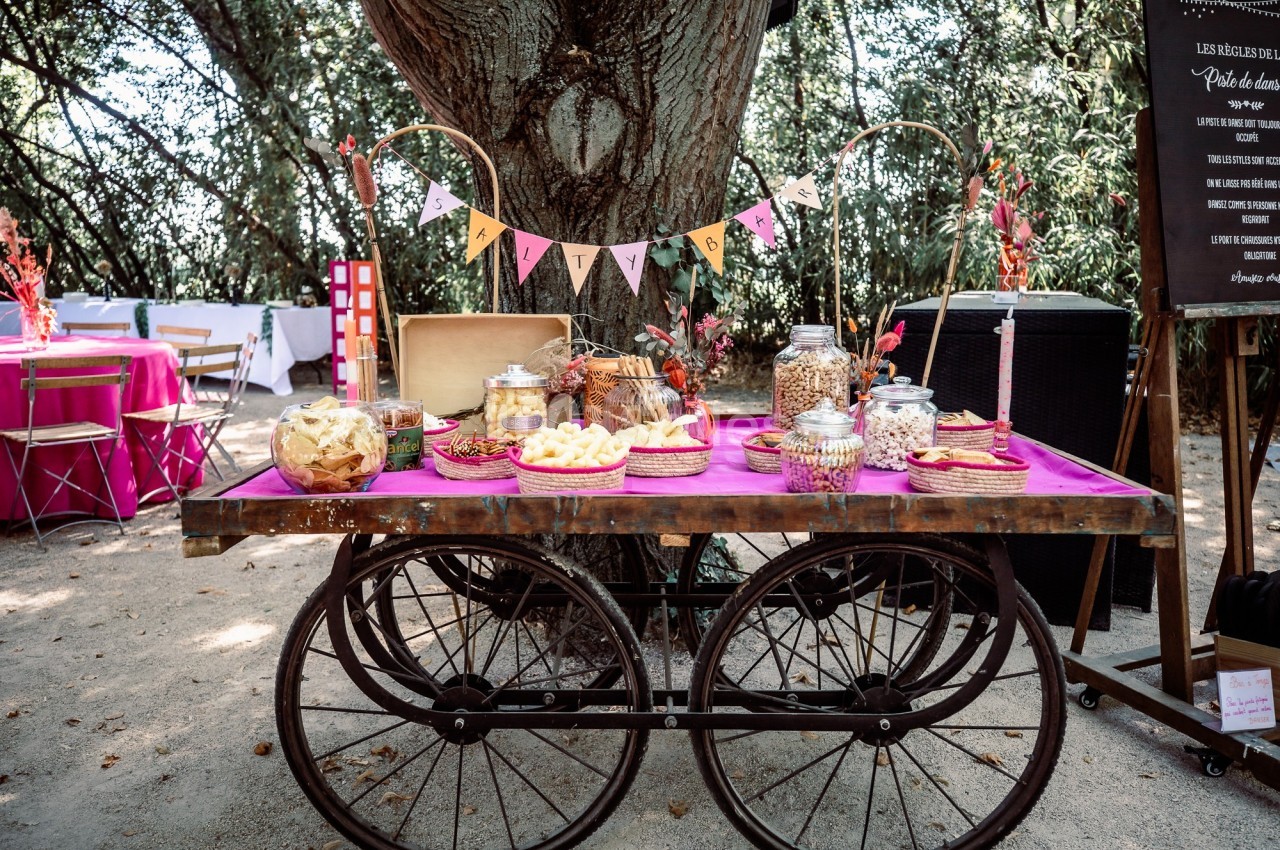 Chariot en bois décoré avec des friandises et snacks disposés sous un arbre dans un cadre extérieur festif.