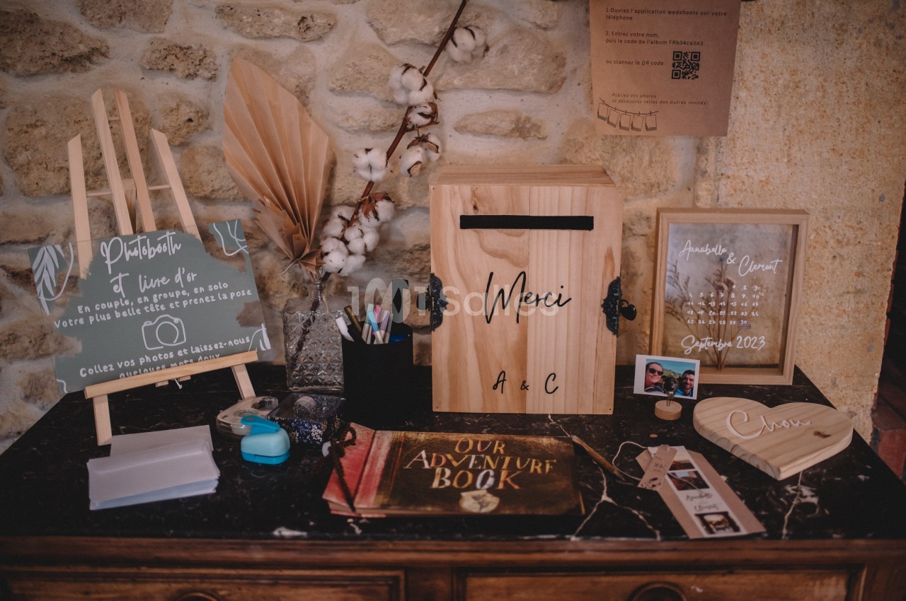 Table décorative avec urne en bois, livre d'or, cadres photo, pancartes et accessoires pour un mariage.