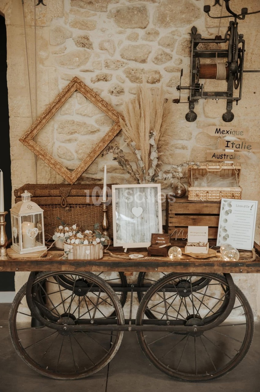 Table en bois sur roues décorée d'objets rustiques, cadres, bougies, fleurs séchées et accessoires vintage contre un mur en…