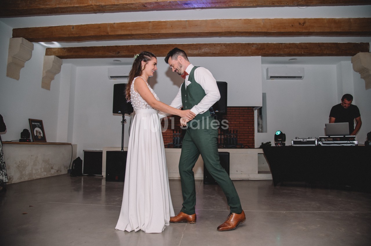 Un couple danse ensemble dans une salle avec un plafond en poutres apparentes et un DJ en arrière-plan.