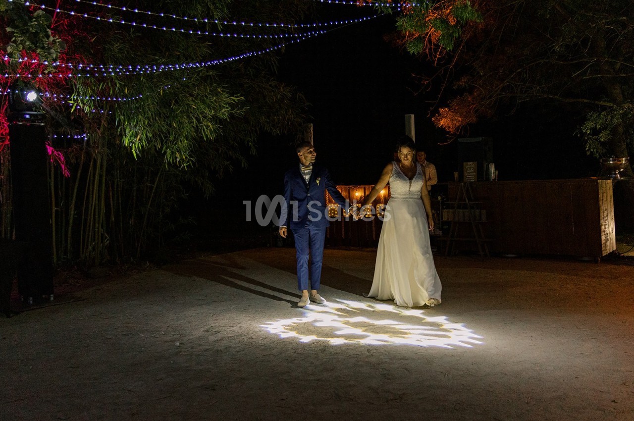 Un couple en tenue de mariage danse sous des guirlandes lumineuses dans un décor extérieur nocturne.