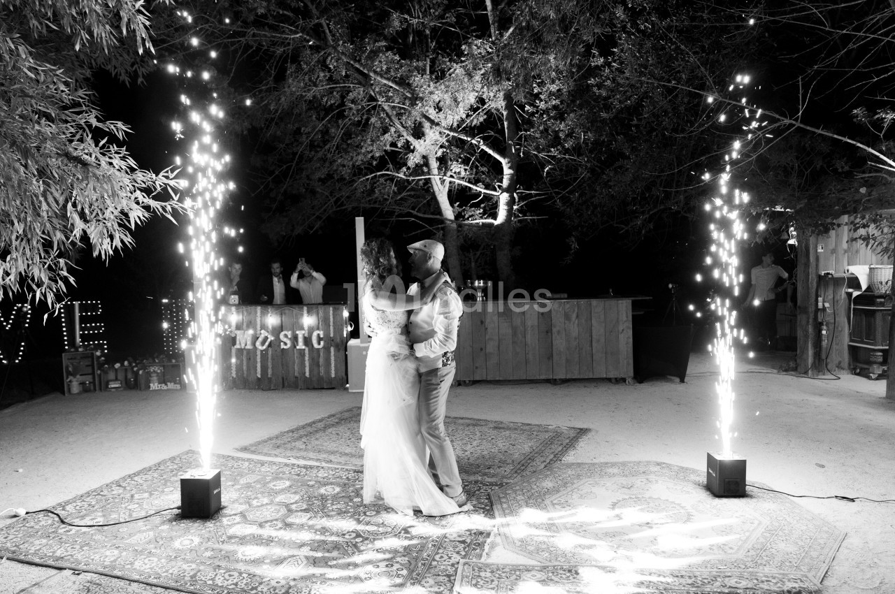 Un couple danse sous des étincelles lumineuses dans un décor extérieur nocturne avec tapis et arbres.