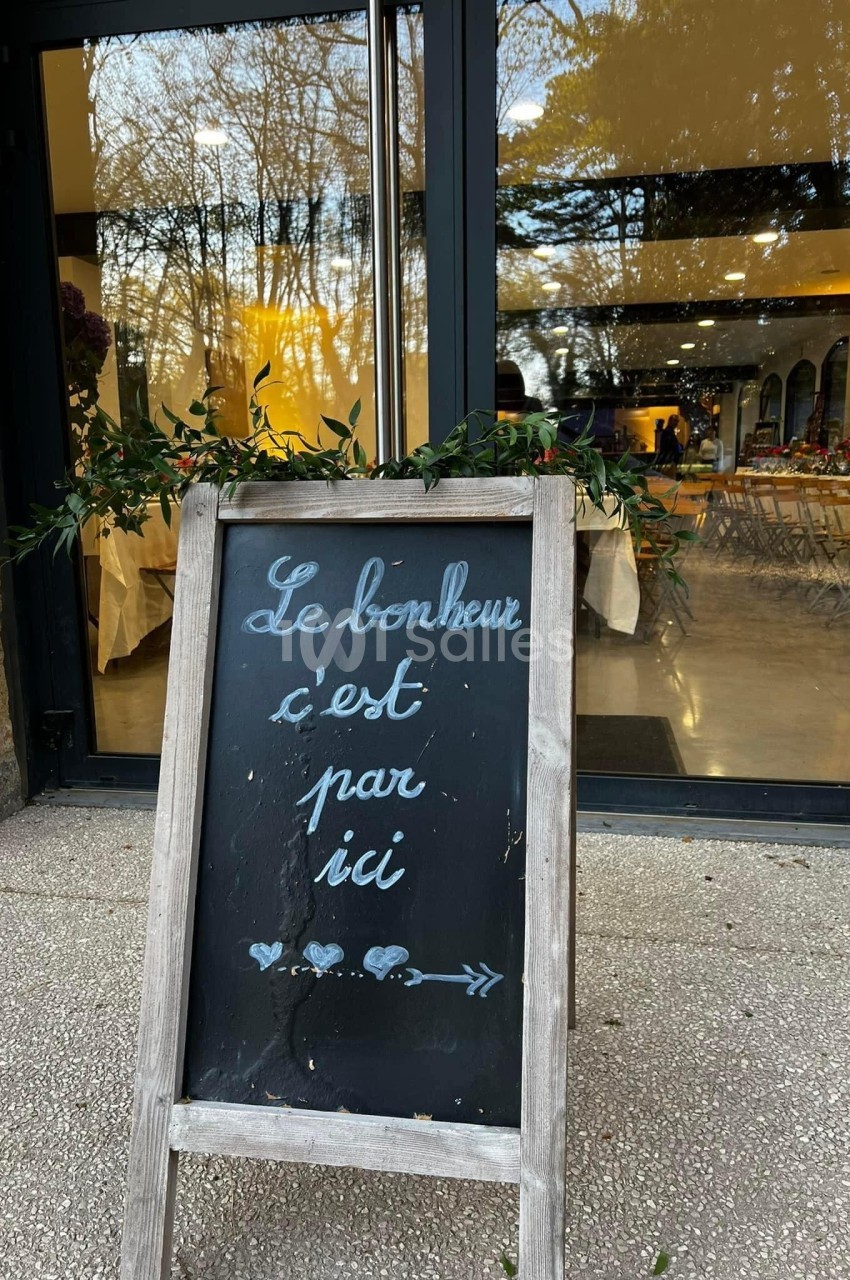 Tableau noir devant une vitrine, inscrit ’Le bonheur c'est par ici’, entouré de feuillage décoratif.