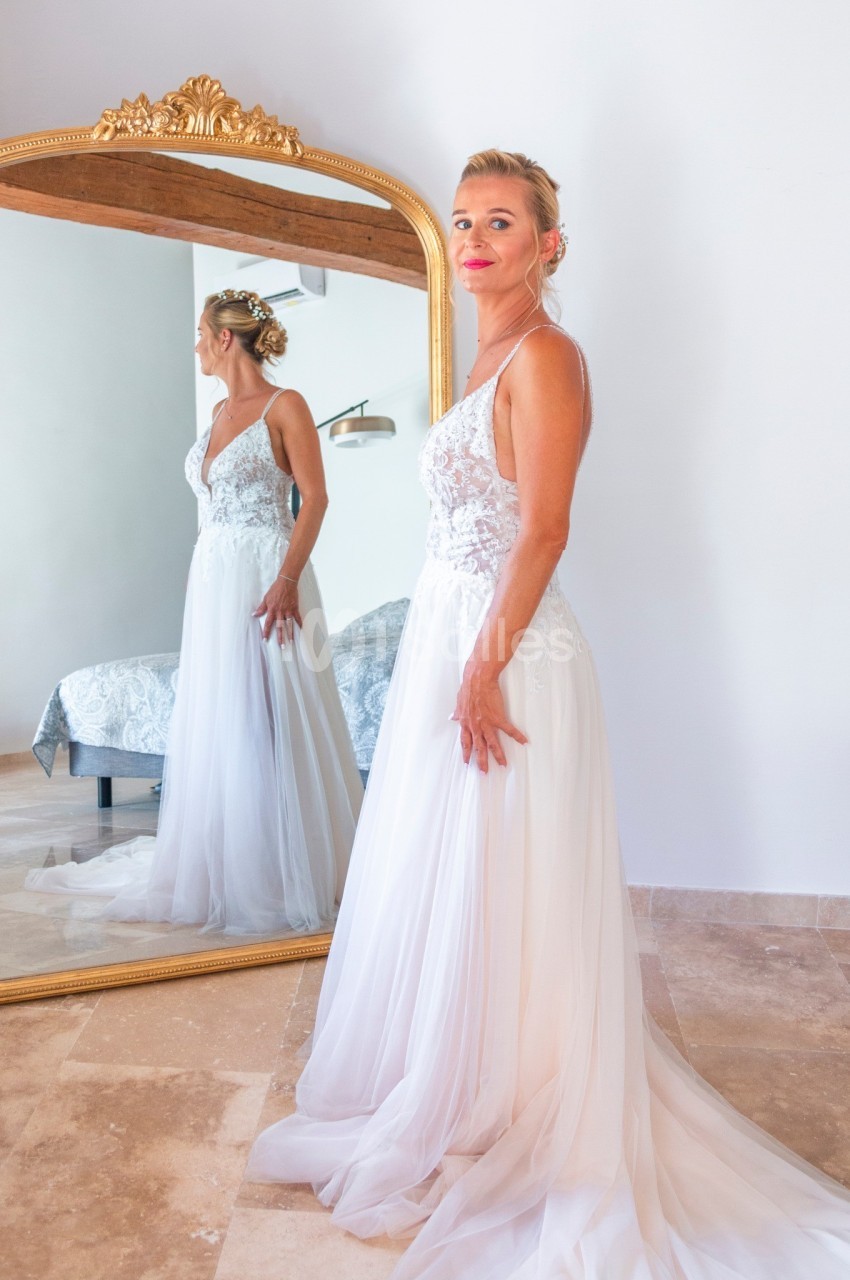 Femme en robe de mariée blanche se regardant dans un grand miroir doré, dans une pièce lumineuse.