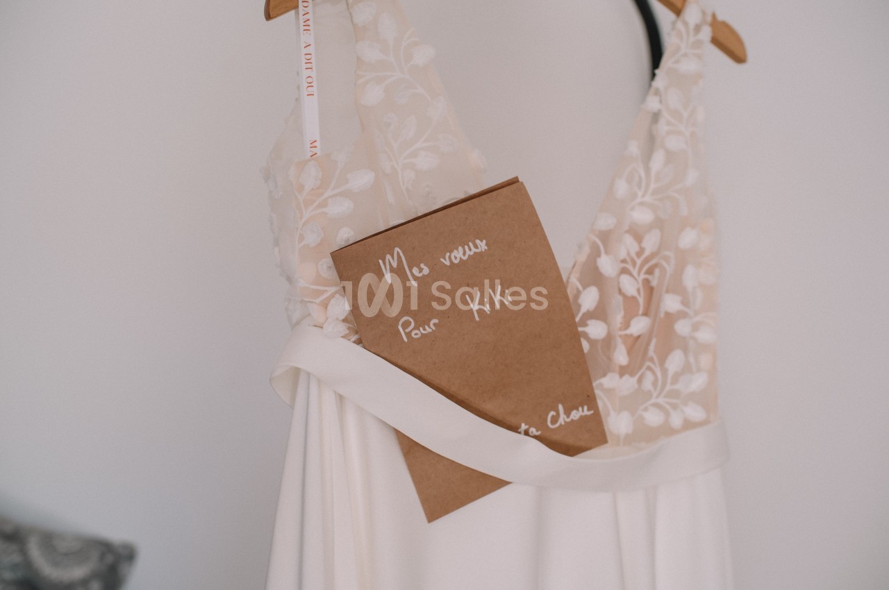 Robe de mariée blanche avec détails en dentelle, sur laquelle est posé un carnet marqué ’Mes vœux pour Kiki’.