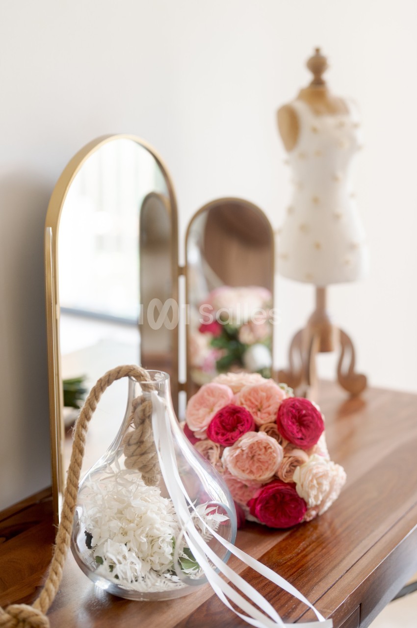 Un vase en verre avec des fleurs blanches, un bouquet de roses et un mannequin décoratif sur une table en bois.