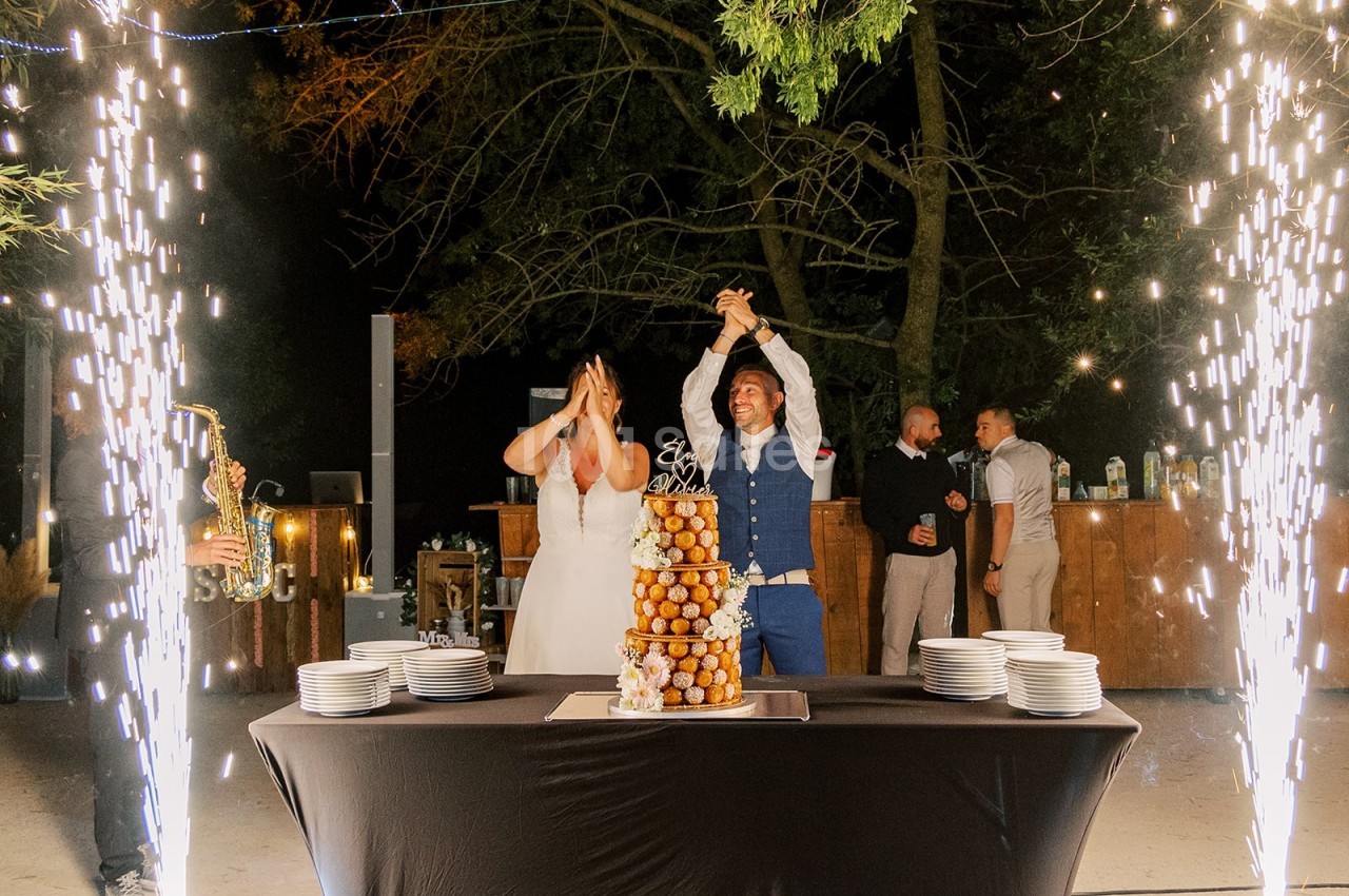 Un couple célèbre son mariage devant une pièce montée éclairée par des étincelles, en extérieur de nuit.