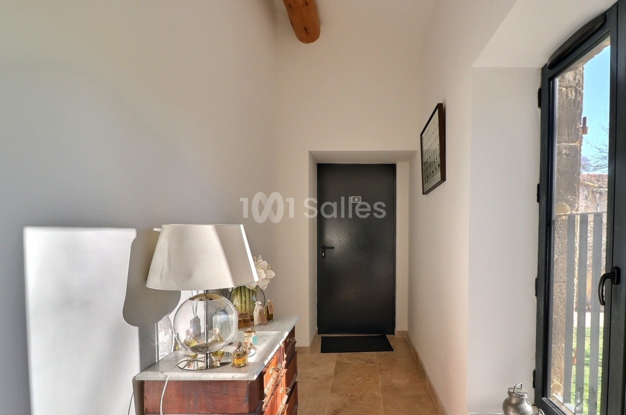Couloir lumineux avec une commode en bois, une lampe, des décorations et une porte noire au fond.