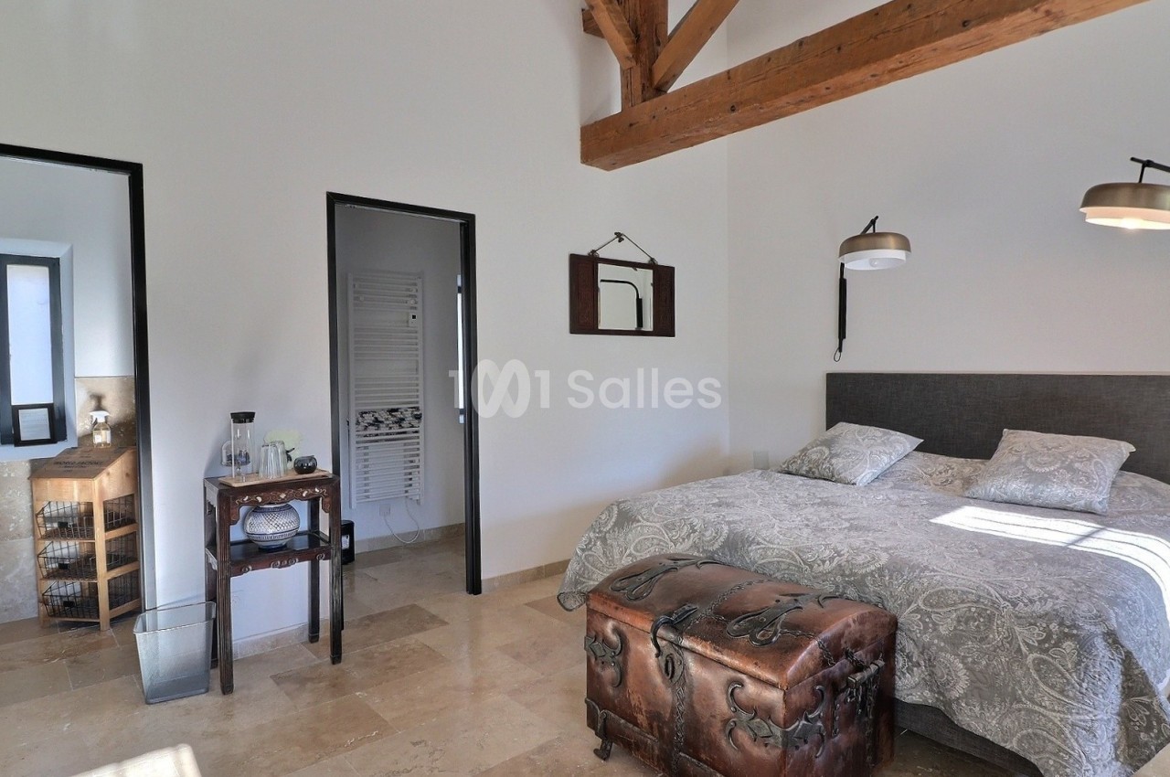 Chambre lumineuse avec lit double, poutres apparentes, sol en pierre et mobilier rustique.