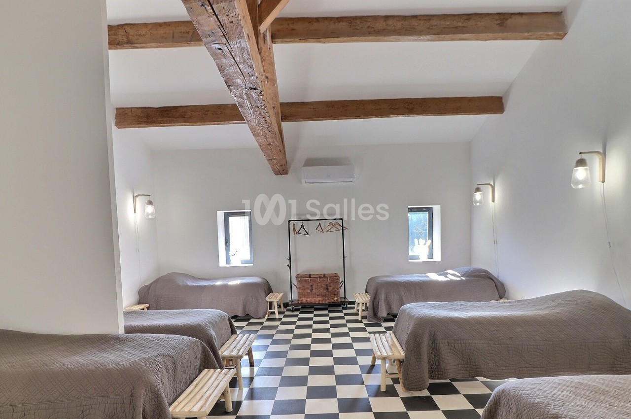 Salle lumineuse avec plafond à poutres apparentes, lits simples alignés, sol en damier noir et blanc.