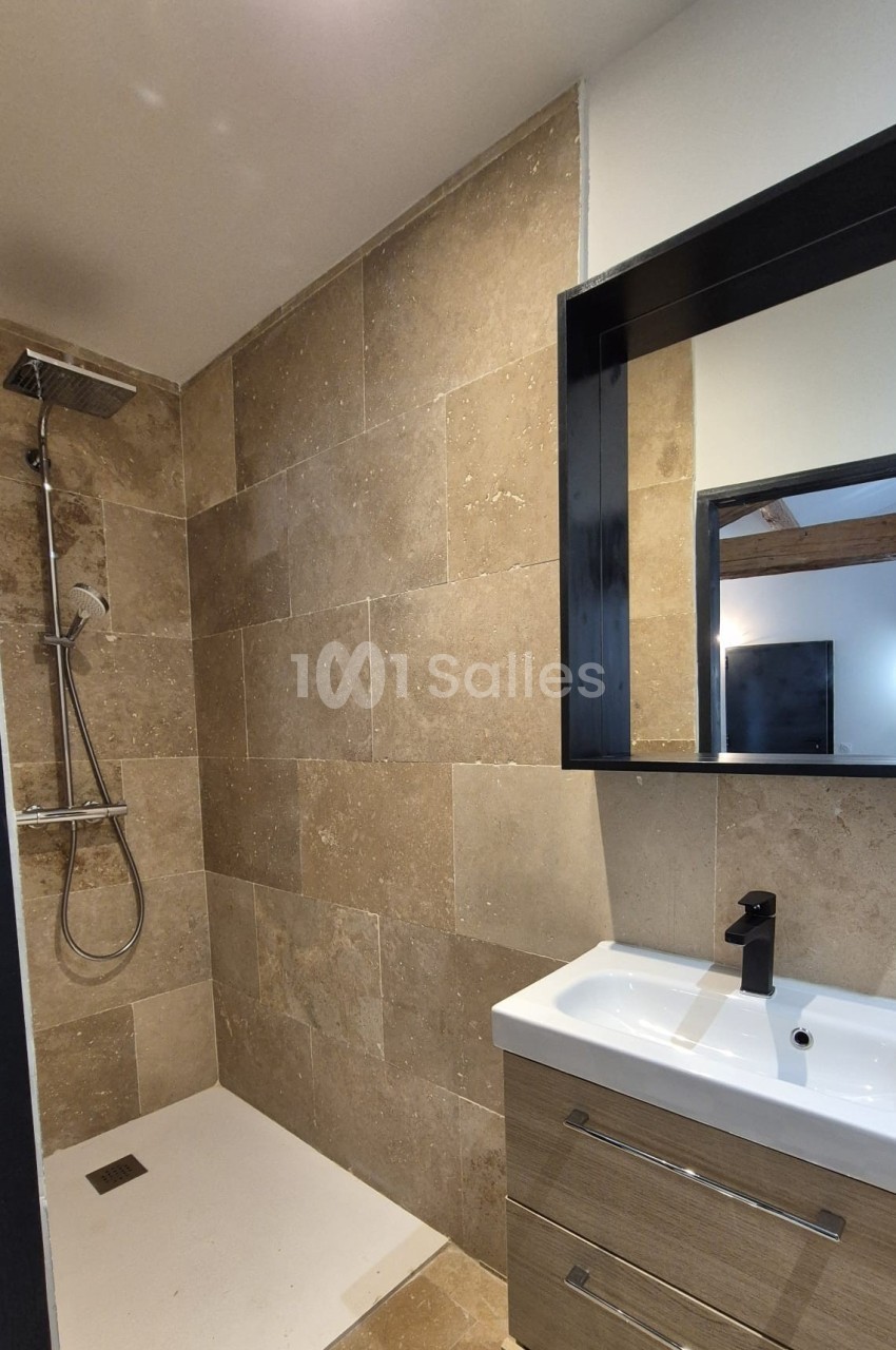 Salle de bain moderne avec douche à l'italienne, carrelage beige, meuble vasque en bois et miroir noir.
