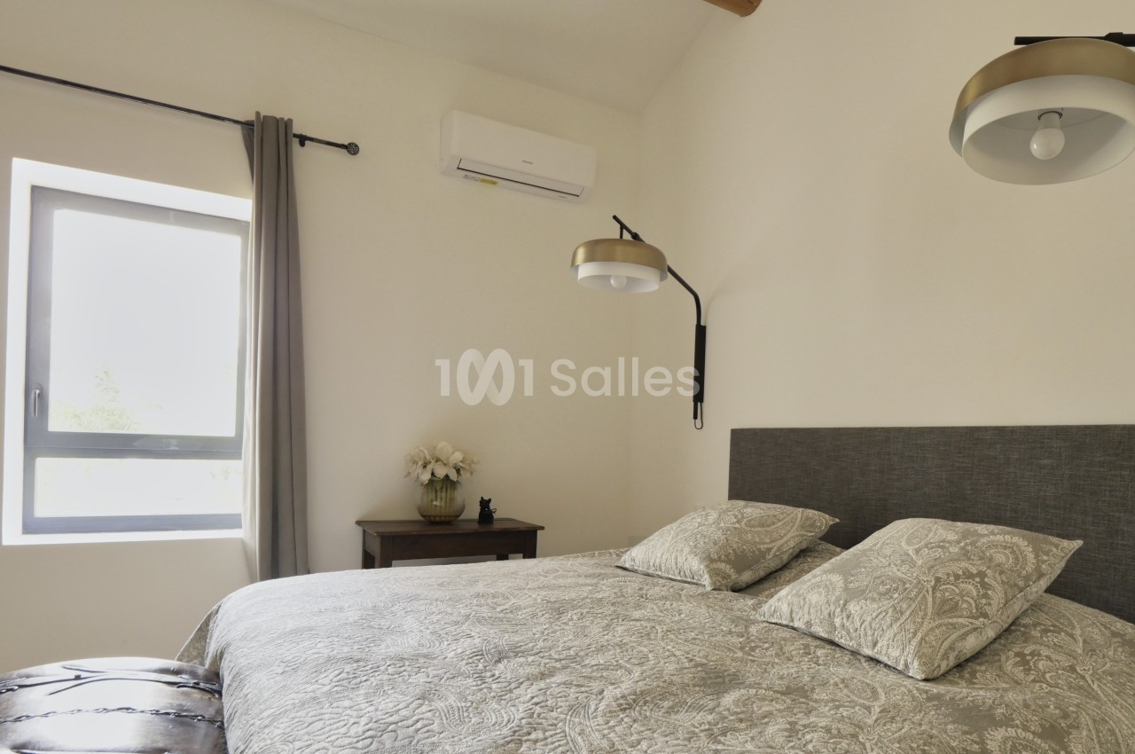 Chambre lumineuse avec lit double, couvre-lit à motifs, lampe murale, fenêtre avec rideaux et table de chevet décorée.