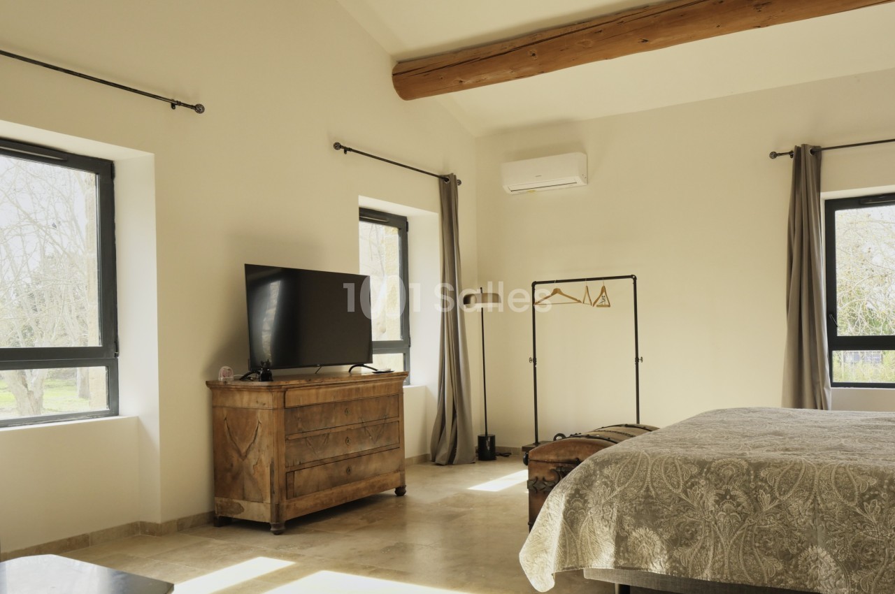 Chambre lumineuse avec lit double, commode en bois, télévision, portant à vêtements et fenêtres donnant sur l'extérieur.