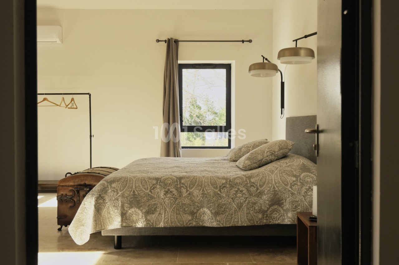 Chambre lumineuse avec un lit double, couvre-lit à motifs, fenêtre, portant à vêtements et appliques murales.