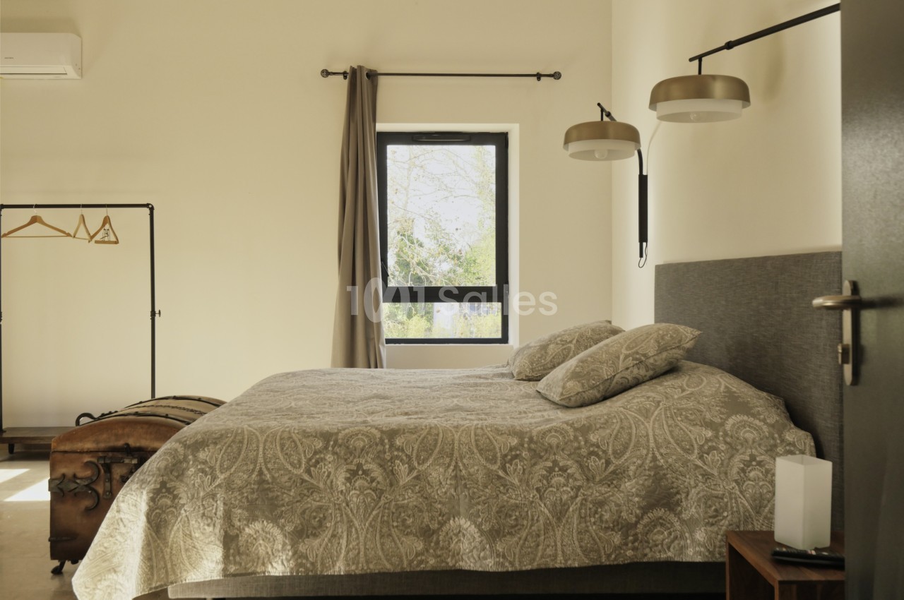 Chambre lumineuse avec un lit double, linge à motifs, fenêtre donnant sur l'extérieur et portant avec cintres.