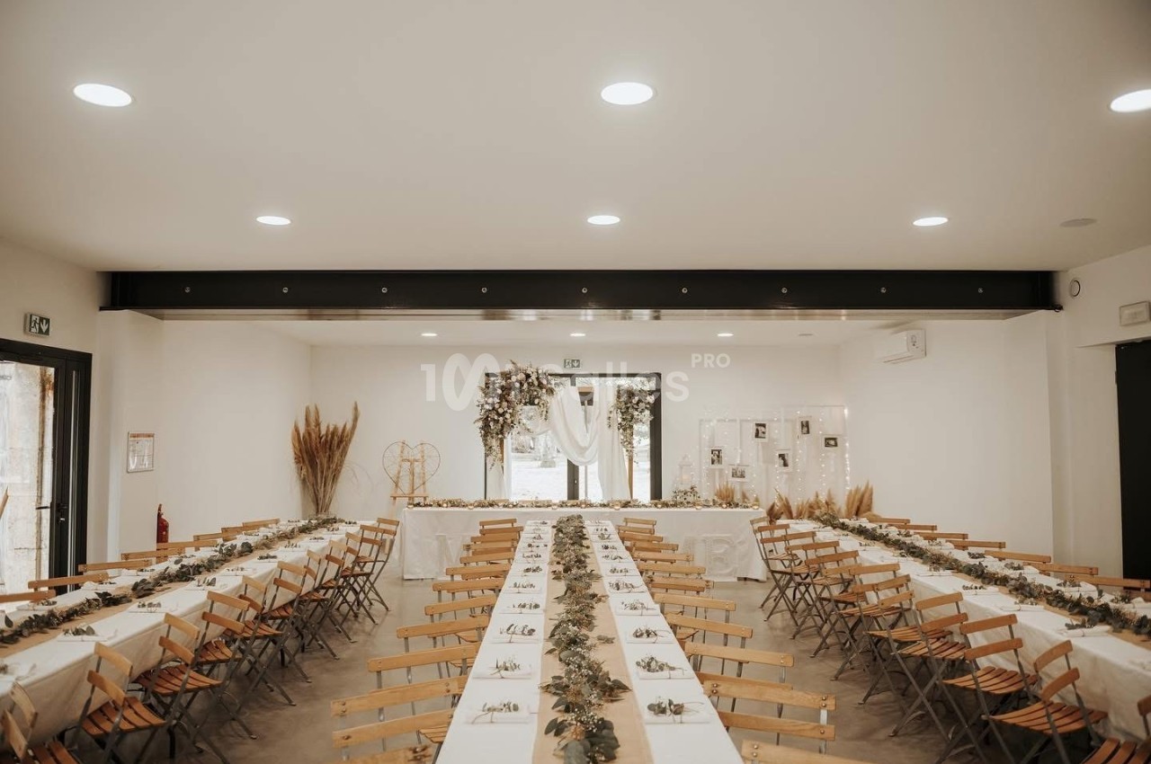 Salle de réception décorée avec des tables alignées, nappes blanches et ornements végétaux, prête pour un événement.