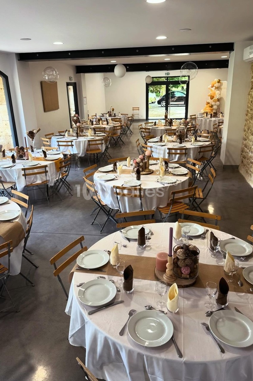 Salle de réception décorée avec des tables rondes dressées, nappes blanches et éléments de décoration champêtres.