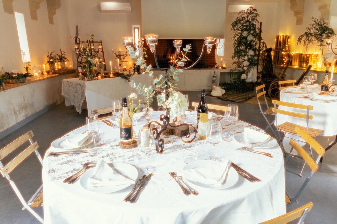 Table dressée avec nappes blanches, couverts, verres et bouteilles de vin, dans une salle décorée avec chandeliers et…