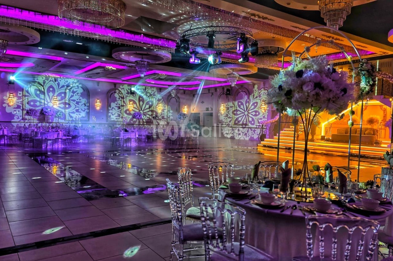 Salle de réception décorée avec des lumières colorées, des tables élégantes et une scène illuminée en arrière-plan.