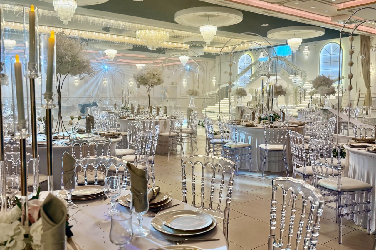 Salle de réception élégante avec tables dressées, chaises transparentes et décorations lumineuses sous des lustres imposants.