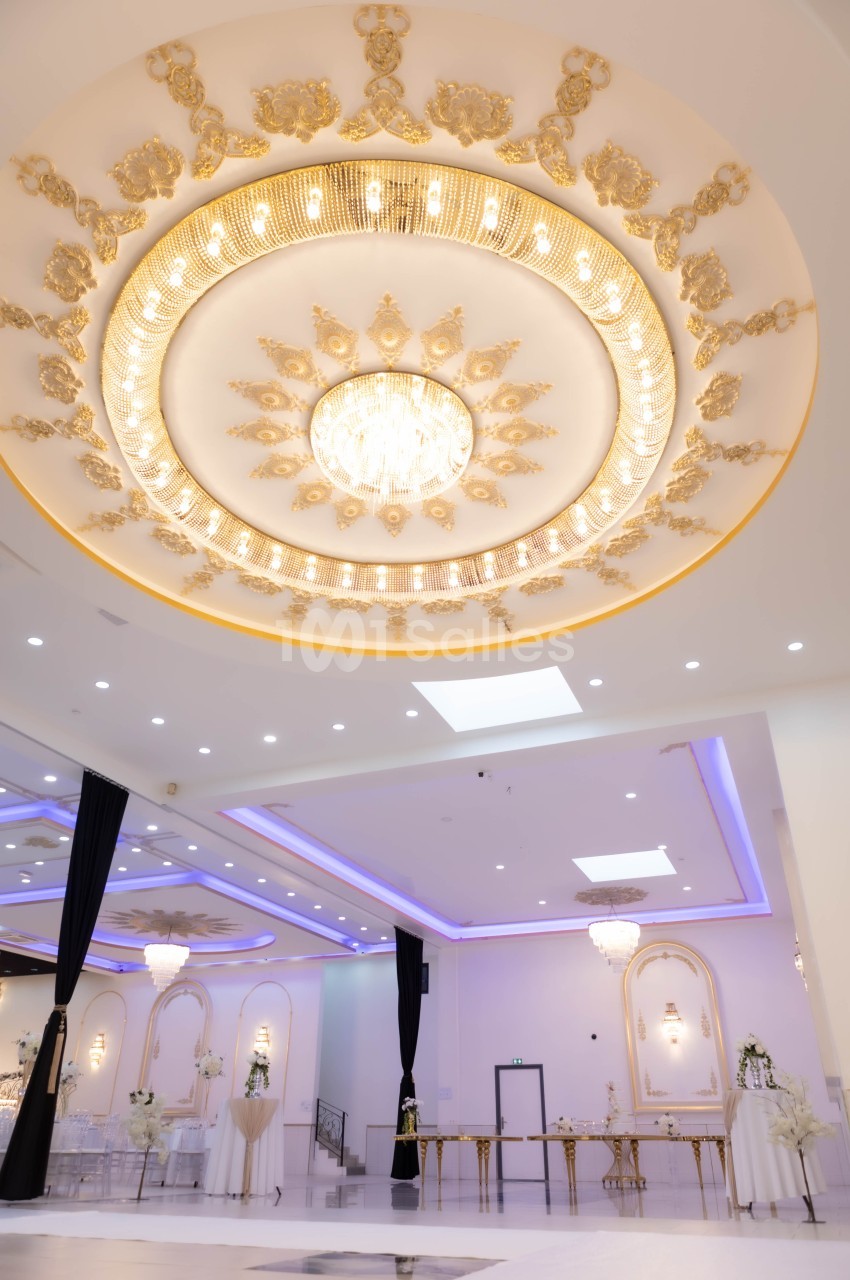 Plafond orné de dorures et d'un grand lustre central dans une salle de réception élégante et lumineuse.