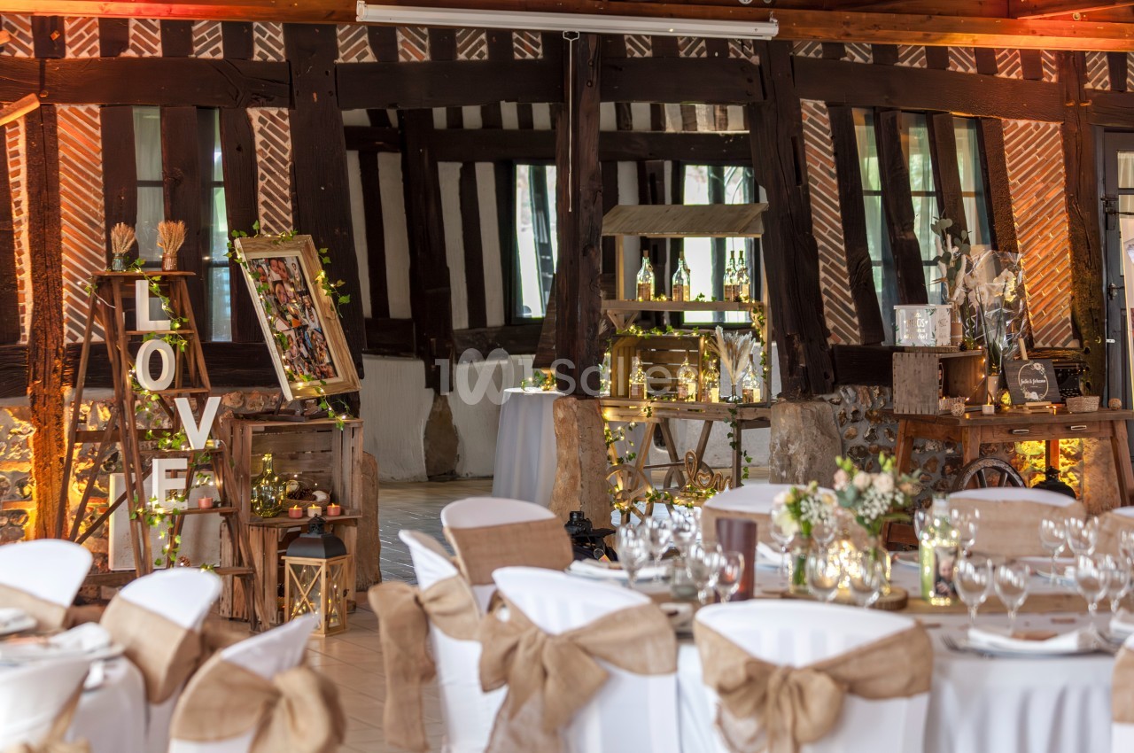 Salle de réception décorée pour un mariage, avec tables dressées, chaises ornées et éléments rustiques en bois.