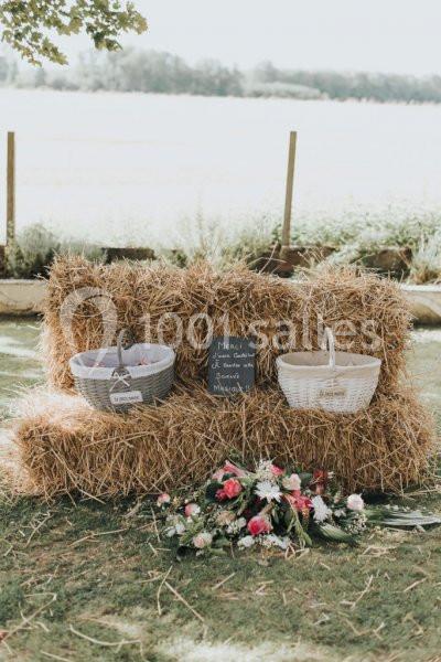 Deux paniers posés sur des bottes de paille avec une ardoise et un bouquet de fleurs au sol, en extérieur.